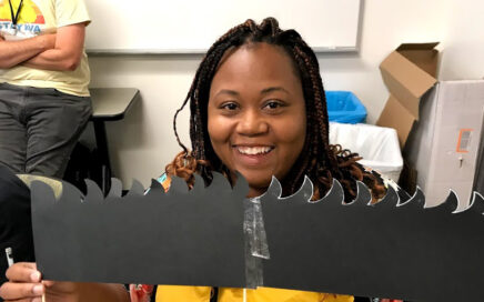 A woman holds a piece of black paper cut in the shape of grass