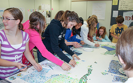 A group of students work on a mosaic on a table