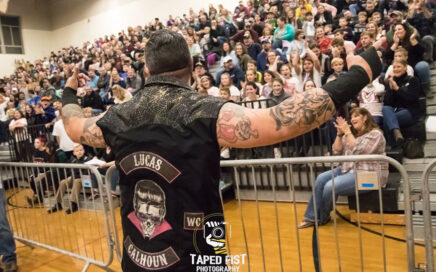 A wrestler addresses a crowd of students sitting in bleachers