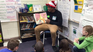 A teenager reads a picture book to younger students in a classroom