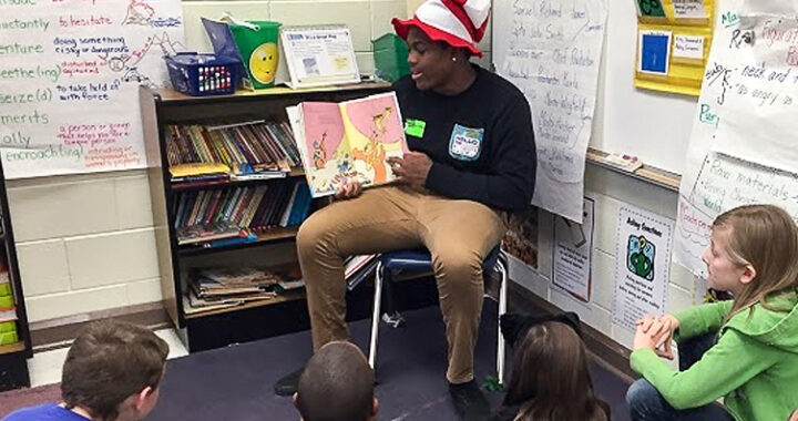 A teenager reads a picture book to younger students in a classroom