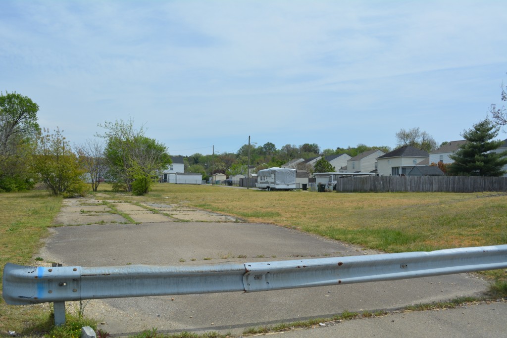 The cracked remains of Old Denny Street sit barricaded and overgrown by vegetation . In the background, new houses have been built, but the community is nothing like it once was. Photo by Garrett Fundakowski.